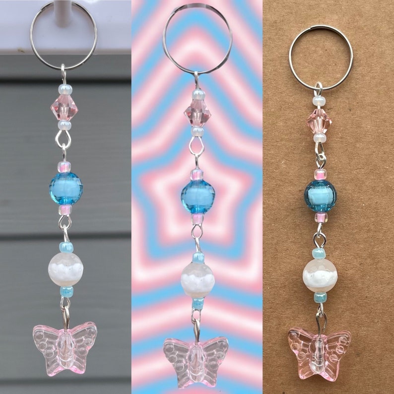 May include: A pink and blue butterfly charm with a silver ring, beads, and a white bead. The charm is hanging from a silver ring.