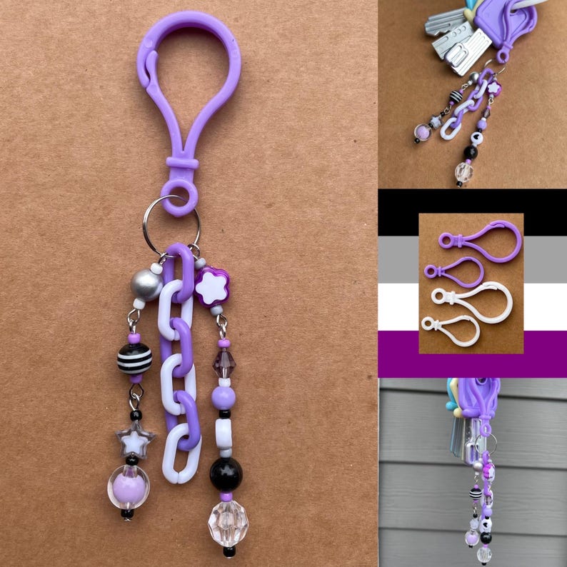 Op de afbeelding: Een paarse sleutelhanger met een karabijnhaak, een zilveren sleutelring en decoratieve kralen. De kralen omvatten zwart-wit gestreepte kralen, witte schakels en stervormige bedels. De sleutelhanger heeft een verscheidenheid aan paarse, zwarte en heldere kralen.