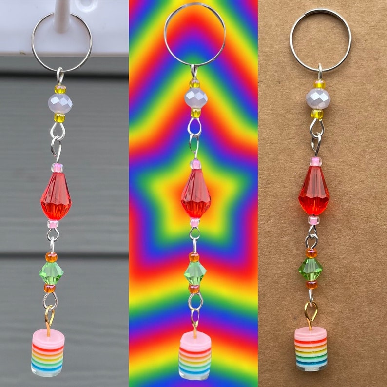 May include: A rainbow layered cake charm with a silver ring, red, green, and pink beads, and a silver chain. The charm is hanging from a silver ring.