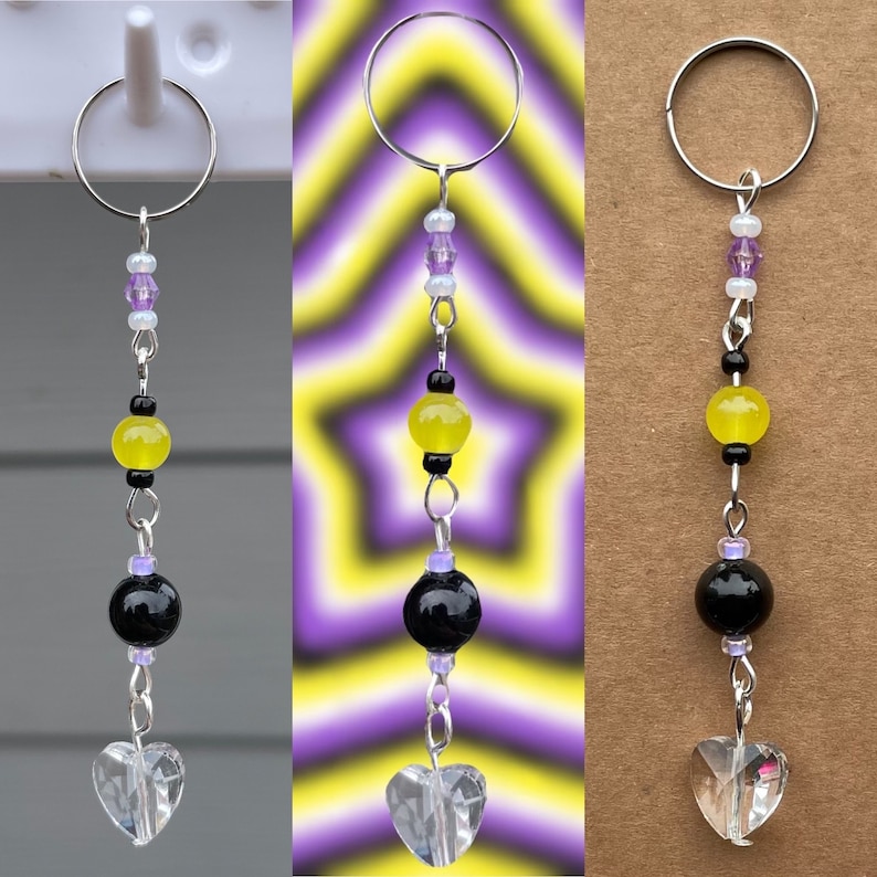 May include: A silver key chain with a yellow, black, and purple beaded charm. The charm features a heart-shaped crystal at the bottom.