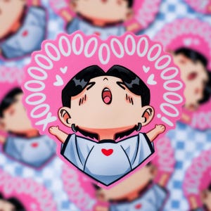 May include: A pink sticker featuring a cartoon character with black hair, wearing a white shirt with a red heart. The character is surrounded by a pink heart-shaped border with the text "10000000000X!".