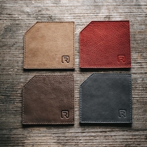 May include: Four leather coasters in different colors: tan, red, brown, and black. Each coaster has a rounded corner and a stitched edge. The letter "R" is embossed in the center of each coaster.