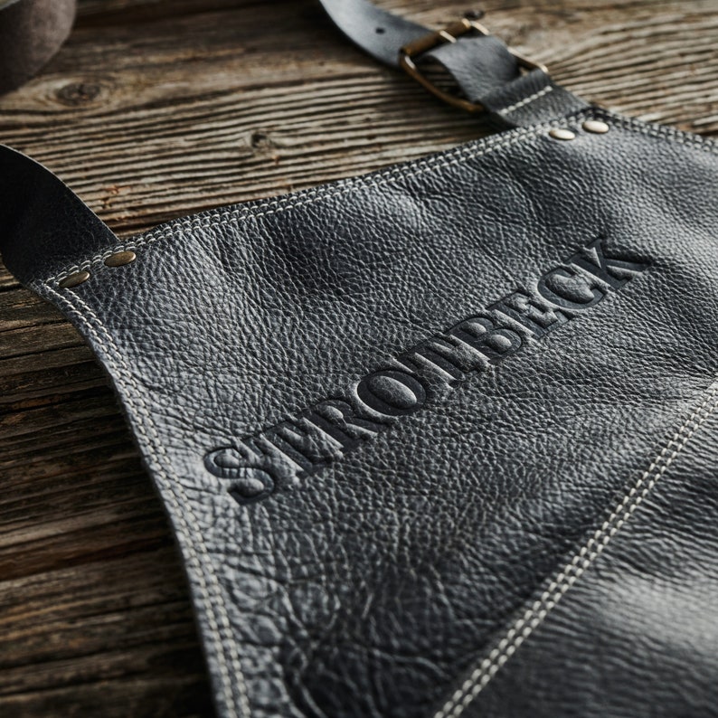 May include: Black leather apron with white stitching and the word "STROWBACK" embossed in the center.