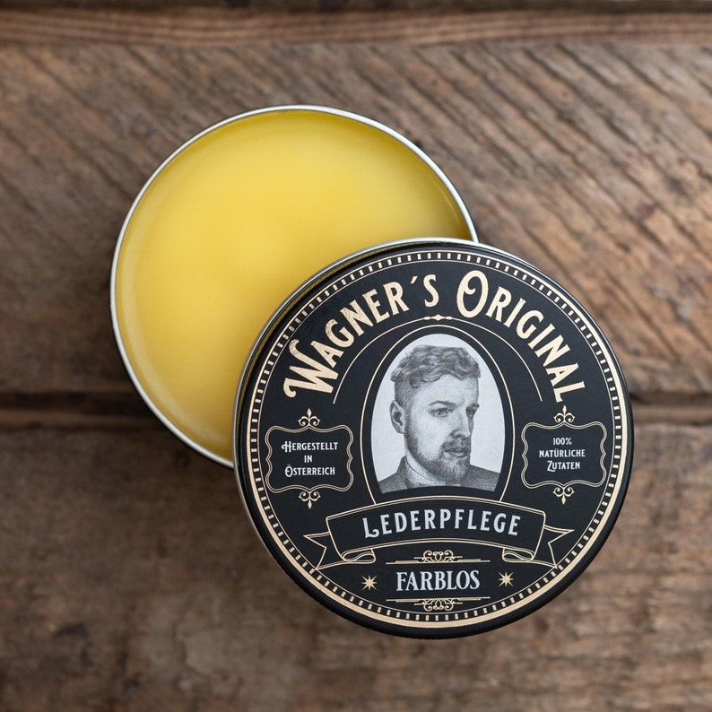 May include: A round tin of leather care product with a black and gold label. The label says "Wagner's Original" and features a man with a beard. The text on the label also says "Hergestellt in &Ouml;sterreich", "100% Nat&uuml;rliche Zutaten", "Lederpflege", and "Farblos".