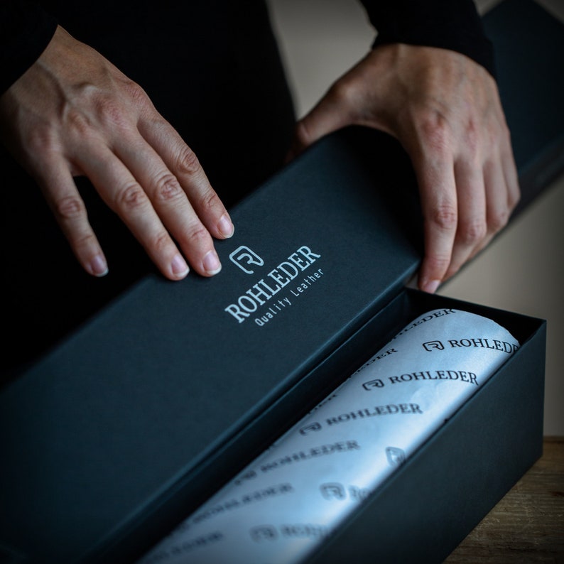 May include: A black box with the text "ROHLEDER Quality Leather" on the lid. The box is open and lined with white tissue paper printed with the same logo.