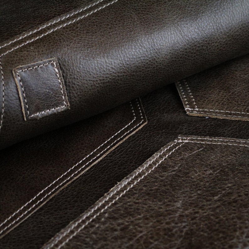 May include: Close-up of brown leather with white stitching. The leather has a textured surface and is folded over to show the stitching on the underside.