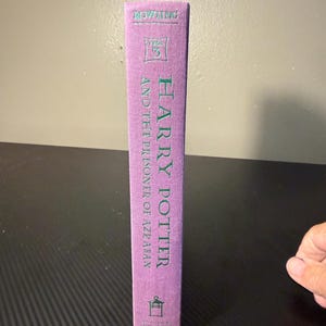 May include: A purple hardcover book spine titled Harry Potter and the Prisoner of Azkaban. The text is printed in teal, featuring the author name Rowling at the top, the number 3 in a square, and a small lantern icon at the bottom of the spine.