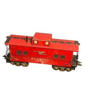 May include: A red toy train caboose with black accents and the word "READING" printed on the side. The caboose has multiple windows and sits on black wheels. The number "92812" is printed below "READING".