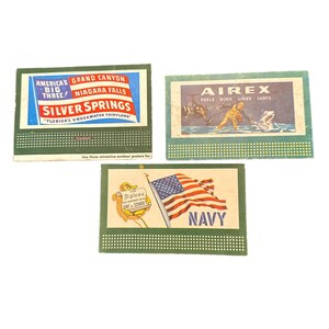 Puede incluir: Tres cajas de cerillas vintage con bordes verdes. Una anuncia las atracciones "America's Big Three", otra promociona los artículos de pesca "Airex", y la tercera presenta una bandera americana ondeando y la palabra "NAVY".