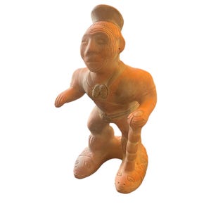 May include: Terracotta figurine of a person wearing a hat and holding a staff. The figurine has detailed facial features and is standing on two feet shaped like snakes.
