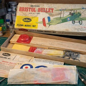 May include: A vintage Bristol Bullet flying model kit by Guillow's. The box shows a green biplane with red, white, and blue markings. The kit contains wooden parts, a red plastic component, and printed instructions. The box reads "BRITISH BRISTOL BULLET world war 1 fighter".