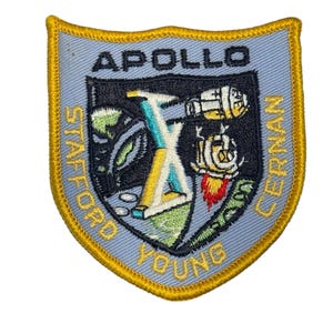 Op de afbeelding: Geborduurde patch met een lichtblauwe achtergrond en een gouden rand. De patch toont het woord "APOLLO" bovenaan, met een centraal ontwerp dat een ruimtevaartuig en andere elementen afbeeldt. De namen "STAFFORD", "YOUNG" en "CERNAN" zijn ook zichtbaar.