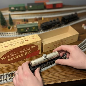 May include: A vintage Silver Streak Deluxe Kit model train set. The kit includes a silver Shell Chemical tank car on tracks, a box, and other train cars. The box reads "Silver Streak Deluxe Kit".