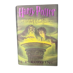Puede incluir: Un libro titulado "Harry Potter y el Misterio del Príncipe" con una cubierta verde y morada. La portada presenta ilustraciones de Harry Potter, Dumbledore y un cuenco brillante. El nombre del autor, J.K. Rowling, está impreso en la parte inferior.