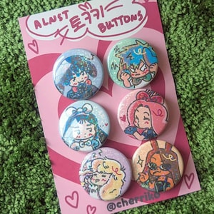 May include: A set of six round buttons with anime-style character illustrations. The buttons are arranged on a pink card with the text "ALNST トキキ= BUTTONS" and the Instagram handle "@cherriki". The background is green.