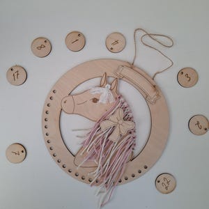 K&ouml;nnte beinhalten: Wanddekoration mit h&ouml;lzernem Pferdekopf, rosa-wei&szlig;em Garnm&auml;hne und Holzschleife. Das Pferd befindet sich in einem Holzreifen mit Banner. Enth&auml;lt kleine Holzscheiben mit Zahlen. Ein dekoratives St&uuml;ck f&uuml;r ein Kinderzimmer.