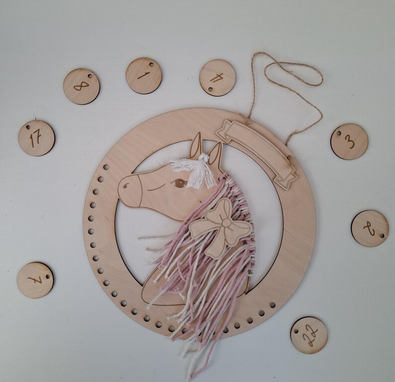 K&ouml;nnte beinhalten: Wanddekoration mit h&ouml;lzernem Pferdekopf, rosa-wei&szlig;em Garnm&auml;hne und Holzschleife. Das Pferd befindet sich in einem Holzreifen mit Banner. Enth&auml;lt kleine Holzscheiben mit Zahlen. Ein dekoratives St&uuml;ck f&uuml;r ein Kinderzimmer.