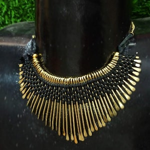 May include: A striking black and gold necklace. The necklace has a woven black base, complemented by gold-coloured metal accents. The gold elements are arranged in a fan-like pattern, creating a bold and eye-catching accessory.