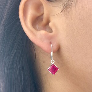 Può includere: Un orecchino in argento con chiusura a monachella, caratterizzato da una pietra preziosa di colore rosso rosato intenso, dal taglio quadrato e incastonata in una semplice montatura metallica. L'orecchino pende da un gancio in argento.