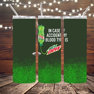 Puede incluir: Un vaso de acero inoxidable verde y negro con un acabado de purpurina verde. El vaso tiene una tapa blanca y una pajita. El vaso tiene un gráfico de una lata de Mountain Dew con una bolsa de IV y el texto "En caso de accidente mi tipo de sangre es Mountain Dew".