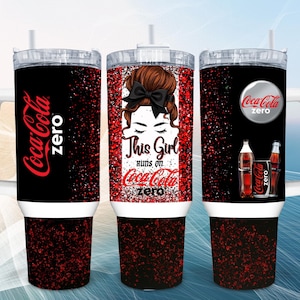 Pode incluir: Um copo de aço inoxidável preto com alça e tampa transparente, apresentando um padrão de glitter vermelho e preto. O design inclui o logotipo da Coca-Cola Zero, uma ilustração de uma pessoa com um coque e laço preto, e o texto This Girl runs on Coca-Cola zero.
