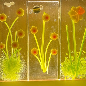 Könnte beinhalten: Drei rechteckige Glasplatten mit gelben Blumen und grünem Laub. Die Blumen haben rote Zentren. Eine Platte zeigt eine kleine Biene. Der Hintergrund ist hellgelb.