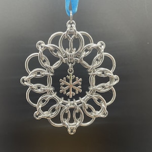 May include: A silver snowflake ornament with a blue ribbon. The snowflake is made of interlocking metal rings and has a smaller snowflake charm hanging from it.