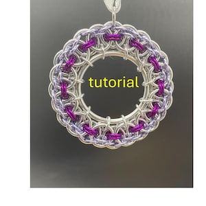 May include: A circular, silver-toned chainmail ornament with purple accents and a silver ribbon for hanging. The word "tutorial" is printed in yellow across the center of the ornament. The chainmail is intricately woven.