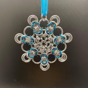 May include: A silver metal snowflake ornament with blue accents and a blue ribbon for hanging. The snowflake design features interlocking rings and is suitable for holiday or winter decor.