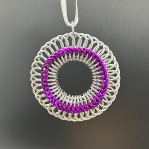 May include: A silver and purple chainmail pendant necklace. The pendant is a circle with a silver outer ring and a purple inner ring.