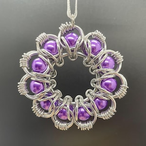 May include: A silver wire ornament with a purple bead design. The ornament is shaped like a flower with a circular center.