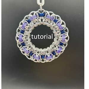 May include: A circular pendant made of silver-colored metal rings, with sections of blue and purple rings. The word "tutorial" is in the center of the pendant. A white ribbon is attached to the top for hanging.