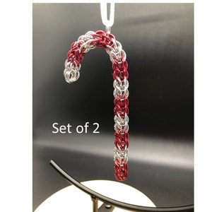 May include: A candy cane ornament made of red and silver metal rings. The ornament is in the shape of a candy cane and has a white ribbon for hanging. The text "Set of 2" is visible.