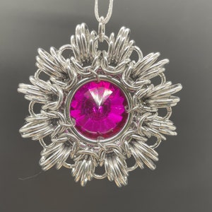 Op de afbeelding: Een zilveren hanger met een roze kristal in het midden. De hanger heeft de vorm van een bloem met meerdere punten.