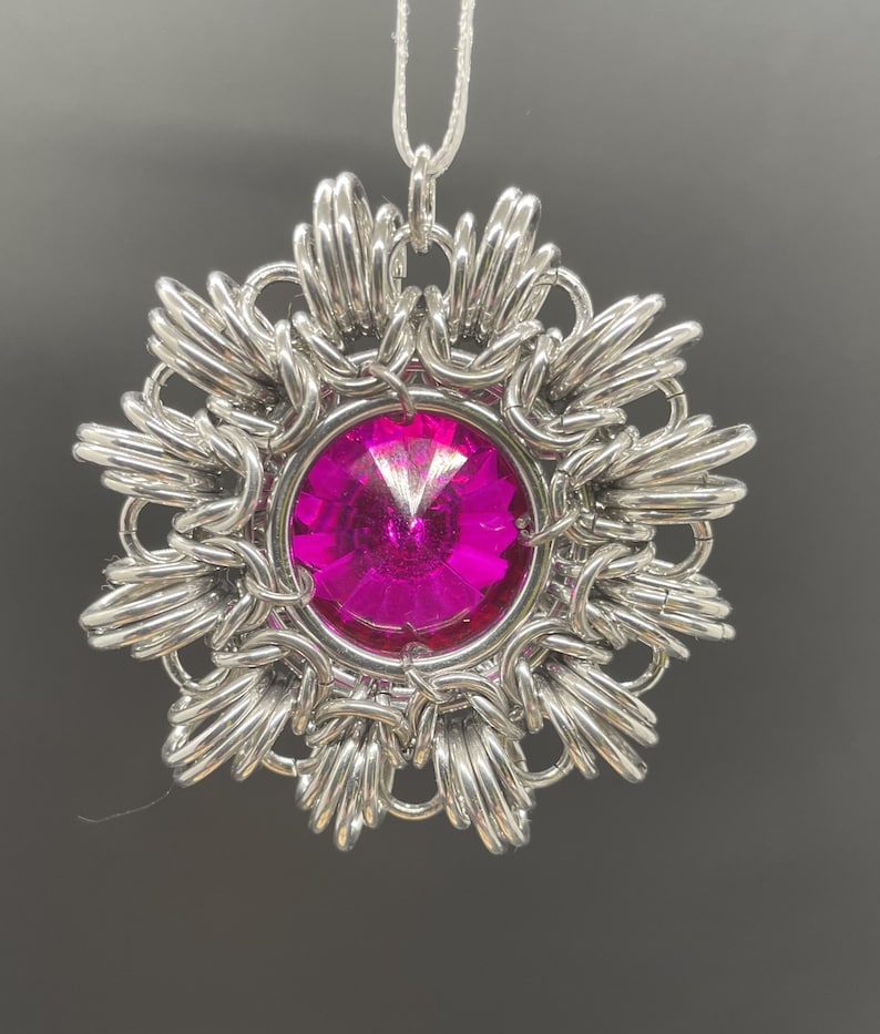 Op de afbeelding: Een zilveren hanger met een roze kristal in het midden. De hanger heeft de vorm van een bloem met meerdere punten.