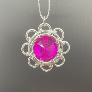 May include: A silver pendant necklace featuring a large, faceted, hot pink gemstone. The gemstone is set within a silver, flower-shaped frame. The necklace chain is also silver and delicate.