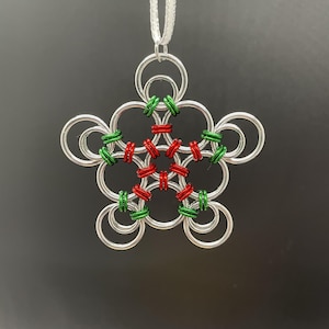 May include: A silver-colored, star-shaped ornament with a white ribbon for hanging. The ornament is made of interlocking rings, with red and green accents in the center. A festive holiday decoration.
