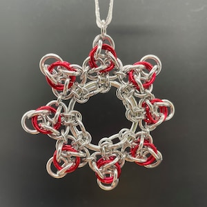 May include: A silver and red star-shaped ornament with a loop for hanging. The star is made of metal rings, with the red rings forming a circle in the center.