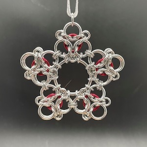 May include: A silver snowflake ornament with red accents. The snowflake is made of metal rings and is designed to hang from a white string.