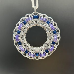 May include: A silver chainmail pendant with a circular design featuring alternating bands of purple and blue.