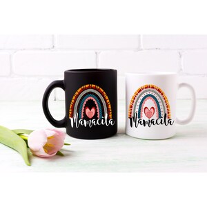 Puede incluir: Dos tazas de caf&eacute; de cer&aacute;mica con un dise&ntilde;o de arco&iacute;ris y el texto "Mamacita" en letras negras. Las tazas est&aacute;n sobre una superficie de madera blanca.