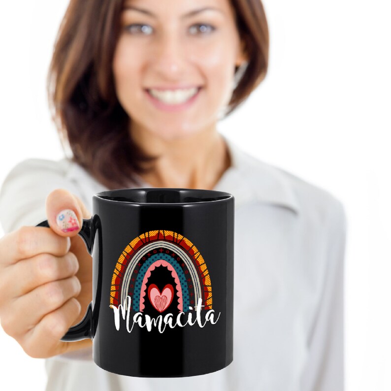Puede incluir: Taza de caf&eacute; de cer&aacute;mica negra con un dise&ntilde;o de arco&iacute;ris y el texto "Mamacita" en blanco. El arco&iacute;ris tiene un coraz&oacute;n en el centro.