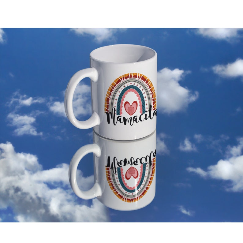 Puede incluir: Taza de cer&aacute;mica blanca con un dise&ntilde;o de arco&iacute;ris y el texto "Mamacita" en letras negras. El arco&iacute;ris est&aacute; formado por rayas rojas, naranjas, amarillas, verdes, azules y moradas con un coraz&oacute;n rosa en el centro.