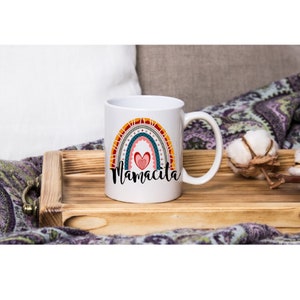 Puede incluir: Taza de cer&aacute;mica blanca con un dise&ntilde;o de arco&iacute;ris y el texto "Mamacita" en negro. El arco&iacute;ris est&aacute; formado por rayas rojas, naranjas, amarillas, verdes, azules y moradas. Hay un coraz&oacute;n rosa en el centro del arco&iacute;ris.
