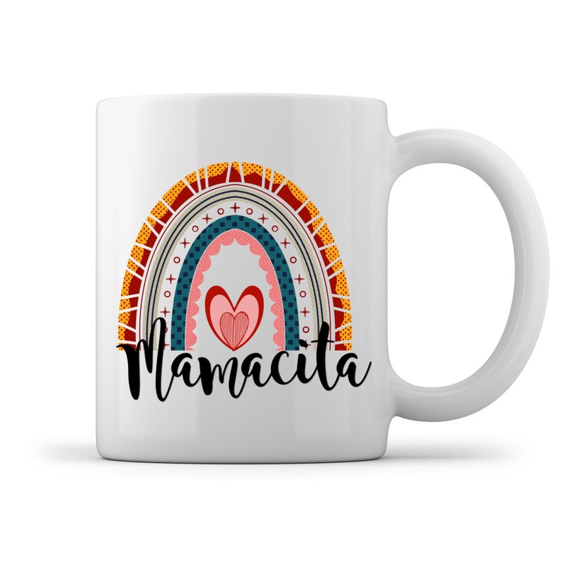 Puede incluir: Taza de cer&aacute;mica blanca con un dise&ntilde;o de arco&iacute;ris colorido y la palabra "Mamacita" en letras negras. El arco&iacute;ris tiene un coraz&oacute;n en el centro.