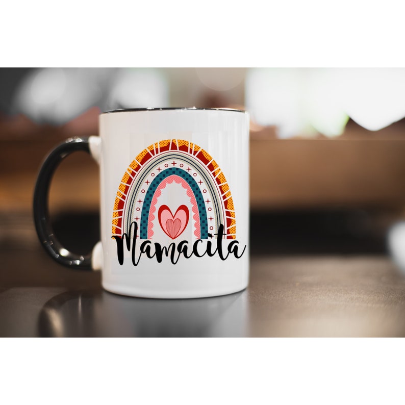 Puede incluir: Taza de cer&aacute;mica blanca con asa negra. La taza presenta un dise&ntilde;o de arco&iacute;ris colorido con un coraz&oacute;n en el centro y el texto "Mamacita" debajo.