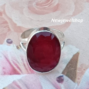 May include: A silver ring featuring a large, oval-shaped, deep red gemstone. The ring is set against a white background.