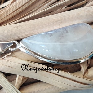 Puede incluir: Un colgante de plata con una piedra preciosa blanca opaca. El colgante tiene forma de l&aacute;grima y tiene un acabado liso y pulido. La piedra preciosa est&aacute; engastada en un bisel de plata y tiene un brillo sutil.