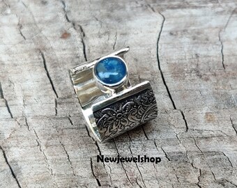 Puede incluir: Un anillo de plata con una piedra preciosa azul engastada en un diseño floral. El anillo es abierto y ajustable.