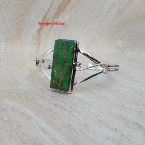 May include: A silver bracelet with a green turquoise stone set in a rectangular frame. The bracelet has a delicate, twisted design.